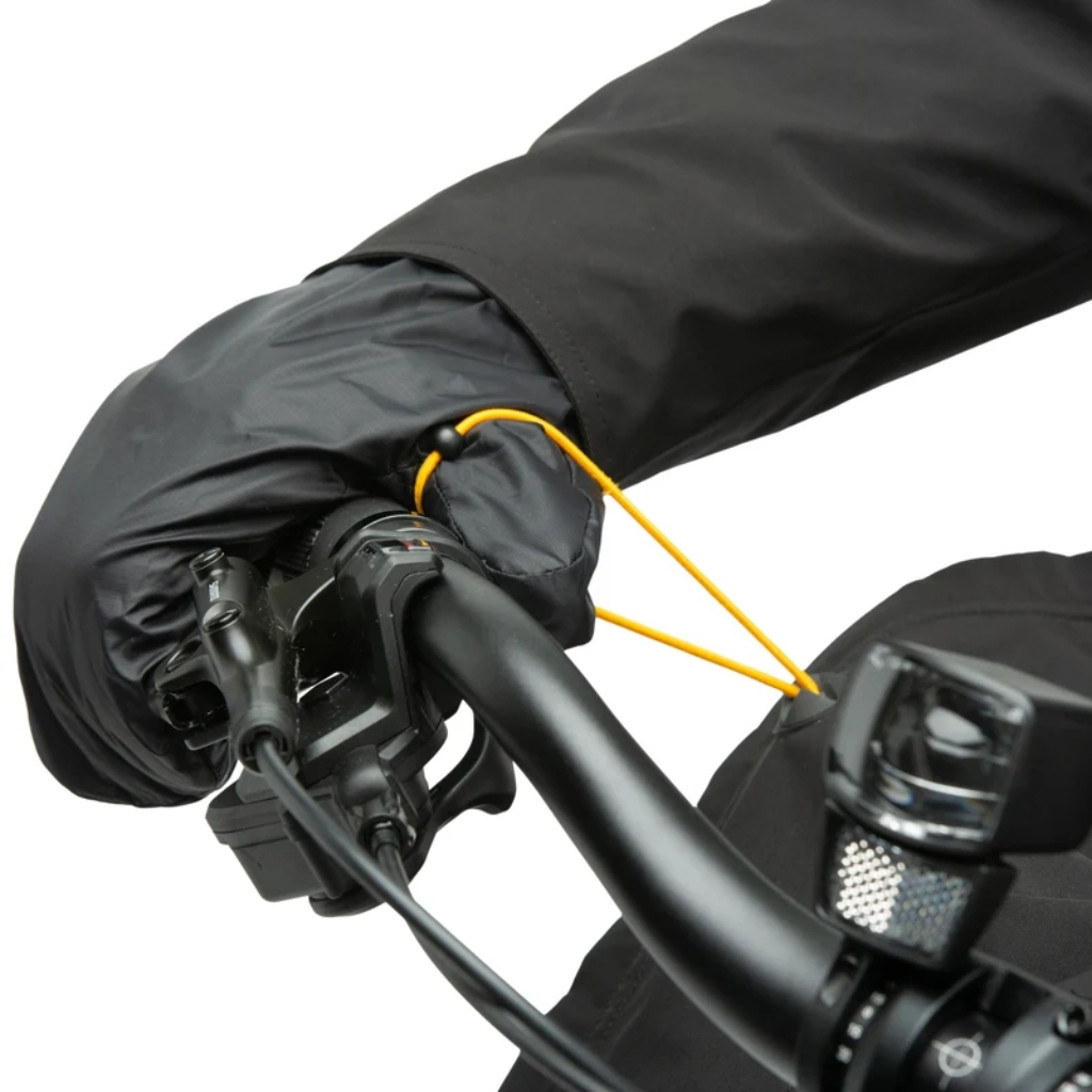 Mains gantées sur guidon de vélo, avec manchon thermique noir et cordon jaune de serrage autour des poignées et freins.