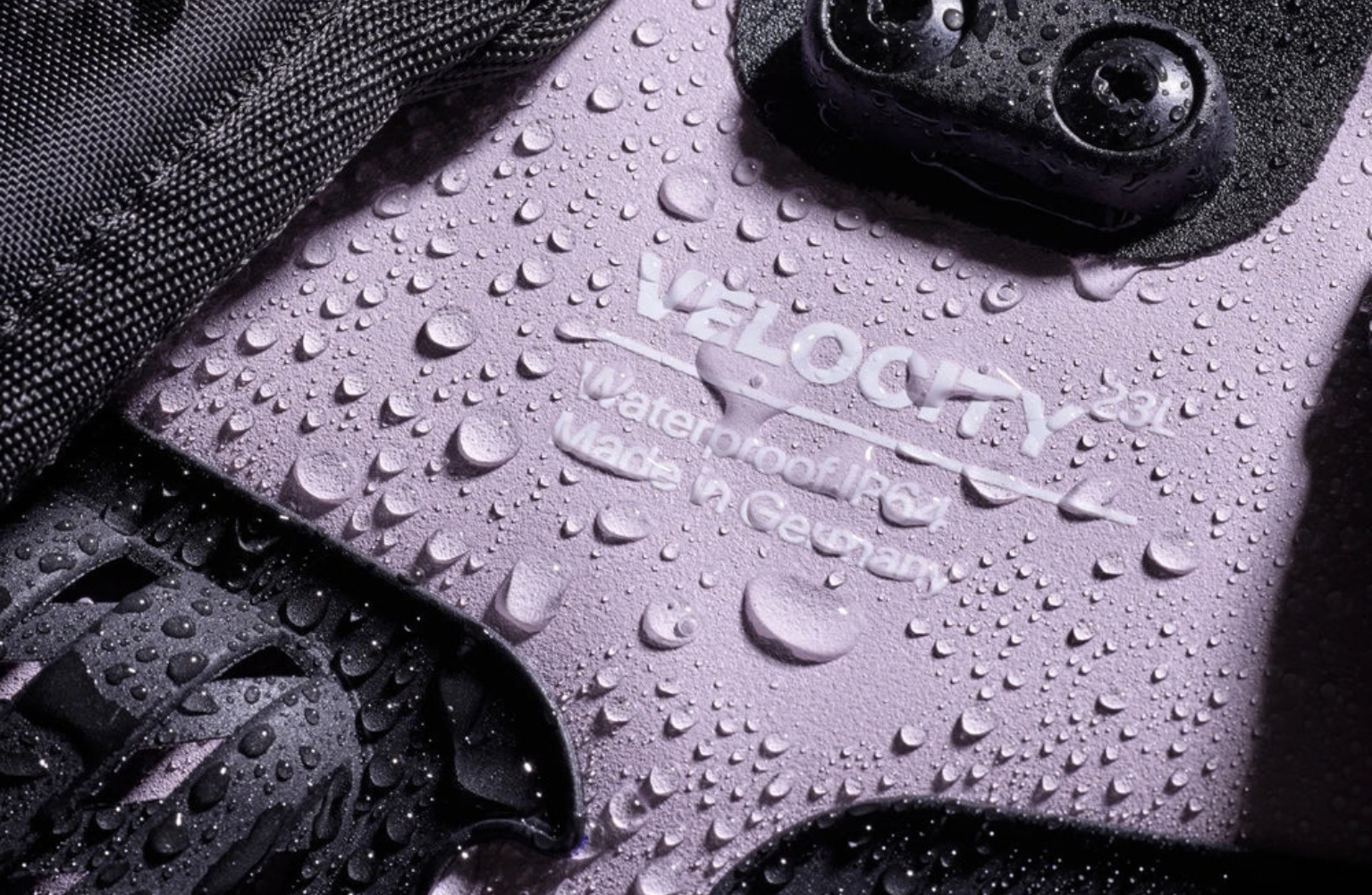 Détail d’un équipement VeloCity Ortlieb noir et lavande, recouvert de gouttes d’eau, avec fixation et tissu technique visibles.