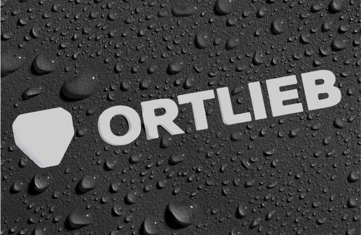 Logo Ortlieb blanc sur fond noir texturé avec gouttes d’eau, évoquant un équipement vélo étanche et résistant.