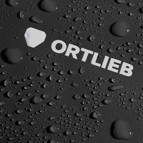 Sac étanche Ortlieb noir, gros plan sur le logo blanc et la surface couverte de gouttes d’eau autres