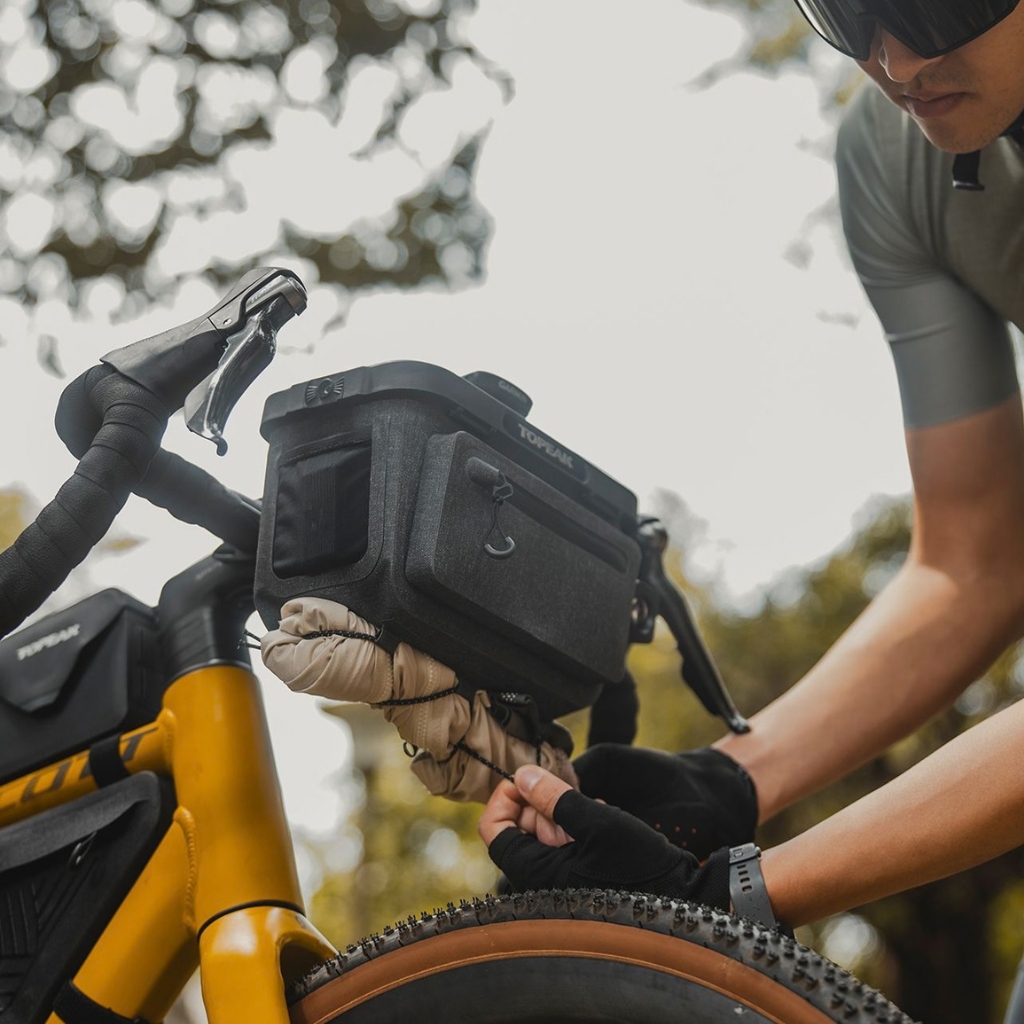 Sacoche de guidon Toppeak noire fixée sur un vélo de route jaune, avec cycliste en train de la fermer en extérieur