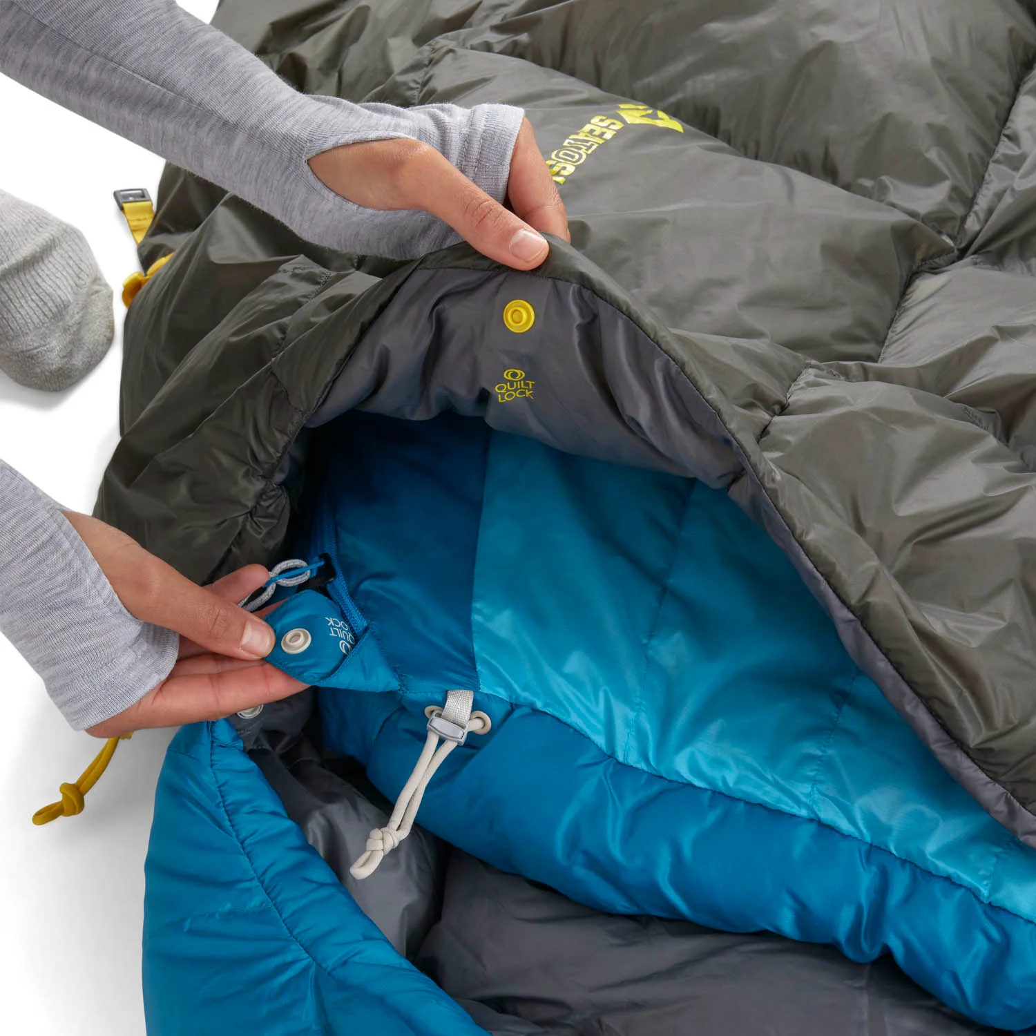 Sac de couchage Quilt Ember ouvert, mains montrant les boutons-pression et le cordon de serrage intérieur QuiltLock.