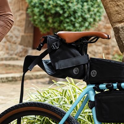 Sacoche vélo Venture Extreme AGU noire fixée sous la selle, avec selle marron et cadre bleu visible, dans un environnement extérieur